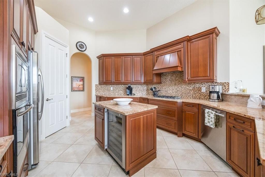 6504 Costa Circle Naples, FL 34113 - Photo 6 of 25 Kitchen with brown cabinetry, arched walkways, premium range hood, appliances with stainless steel finishes, and wine cooler