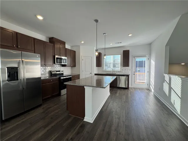 a large kitchen with a center island wooden floor stainless steel appliances and cabinets