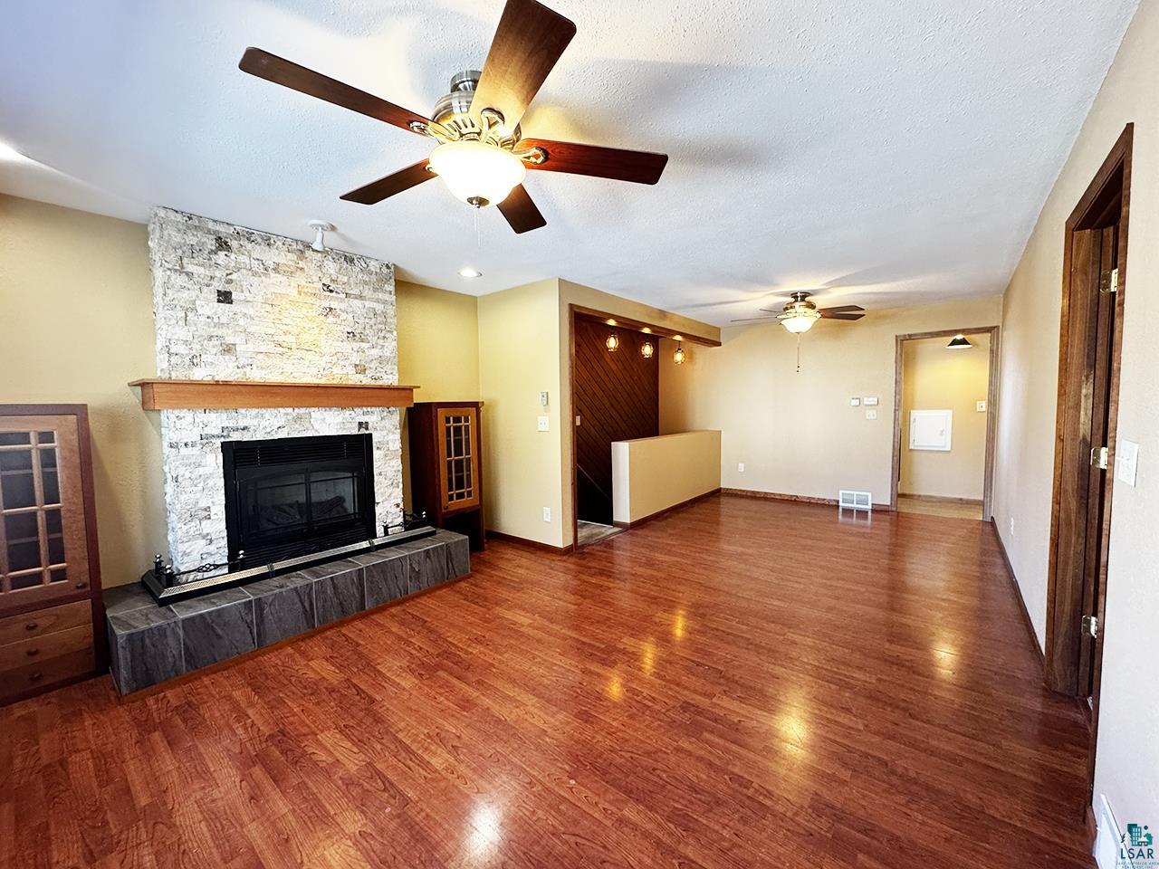 811 7th Street North Virginia, MN 55792 - Photo 12 of 37 Unfurnished living room featuring dark wood-style floors, a ceiling fan, a tiled fireplace, and a textured ceiling