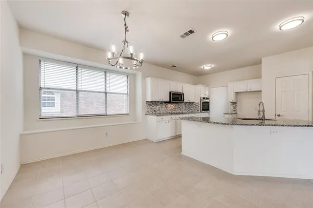 a large white kitchen with granite countertop a stove a sink a refrigerator and white cabinets with wooden floor