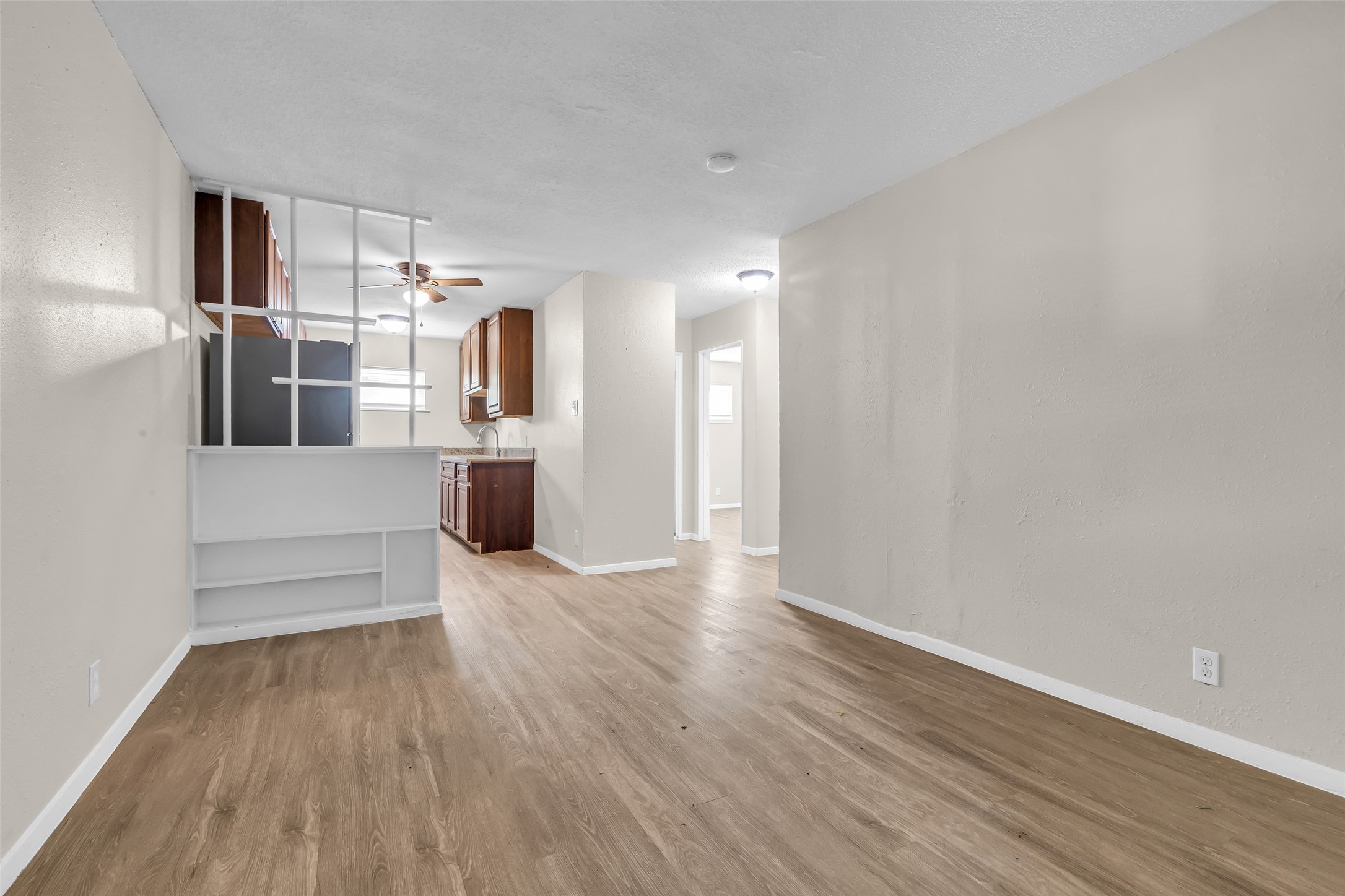 4706 Yellowstone Boulevard, Unit 21 Houston, TX 77021 - Photo 13 of 24 This photo showcases a bright, open living space with vinyl plank flooring, neutral walls, and a view into a kitchen with dark cabinetry. A ceiling fan and built-in shelving add functionality and style.