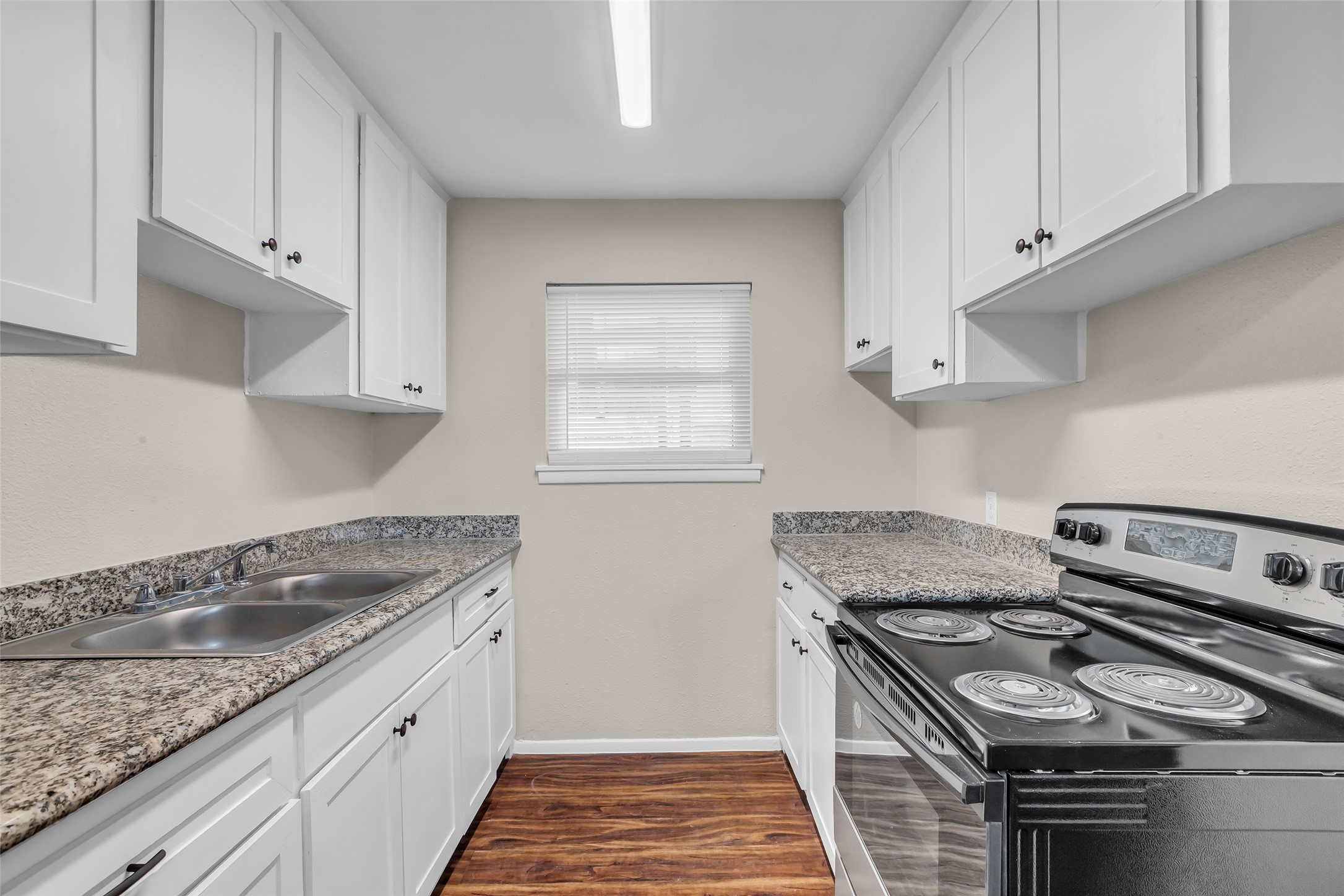4706 Yellowstone Boulevard, Unit 21 Houston, TX 77021 - Photo 18 of 24 This kitchen features granite and or quartz countertops, neutral cabinetry, and a stainless steel electric stove. It has a compact layout with a double sink and a small window for natural light, complemented by wood-style flooring.
