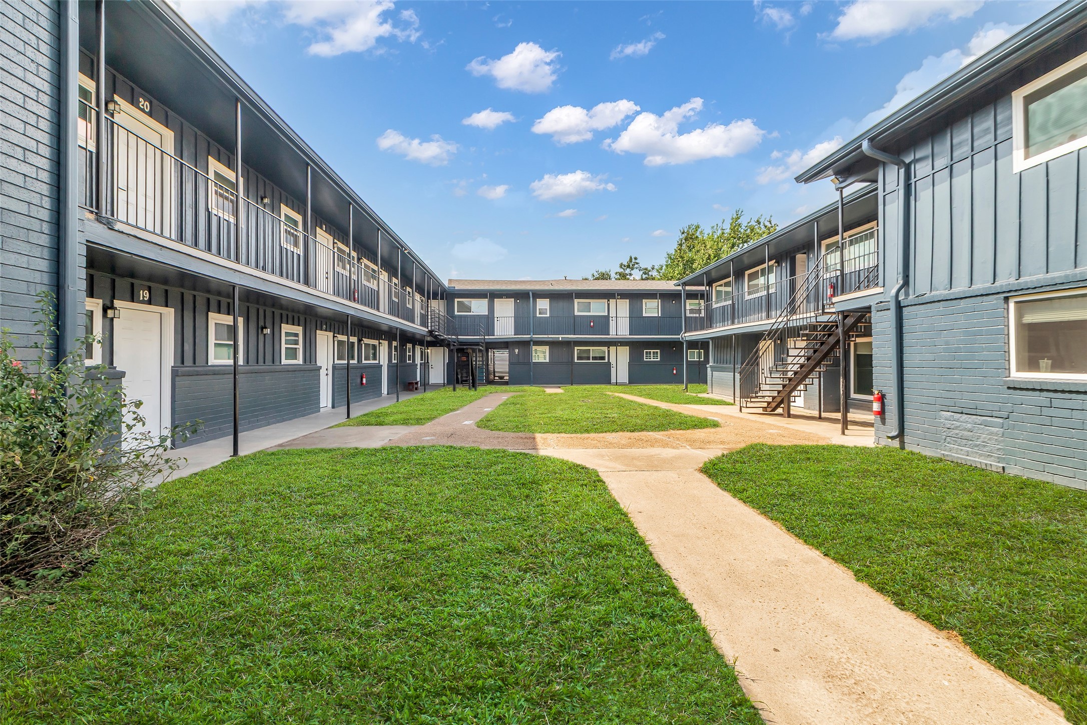 4706 Yellowstone Boulevard, Unit 21 Houston, TX 77021 - Photo 6 of 24 This photo shows a two-story apartment complex with a central grassy courtyard and a clear blue sky. The building features an exterior walkway on the second floor and stairs for access.