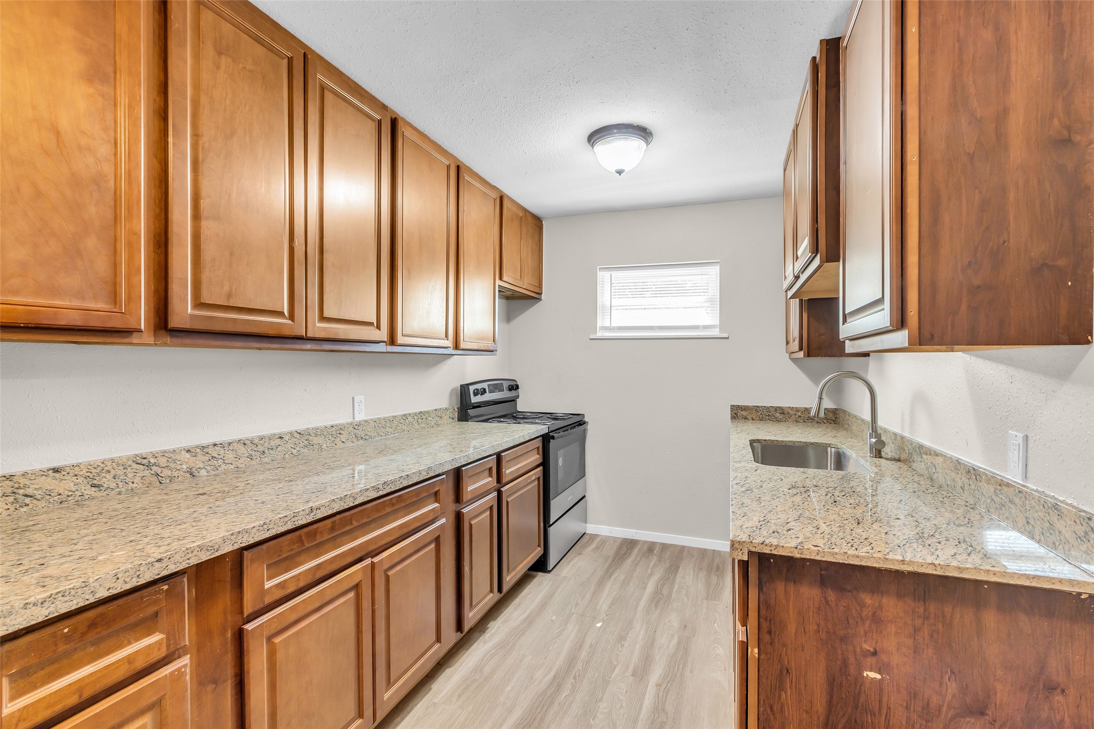 4706 Yellowstone Boulevard, Unit 21 Houston, TX 77021 - Photo 8 of 24 This kitchen features elegant wooden cabinets, granite and or quartz countertops, and a modern appliance set. It's well-lit with natural light from a small window, offering a warm and inviting atmosphere.