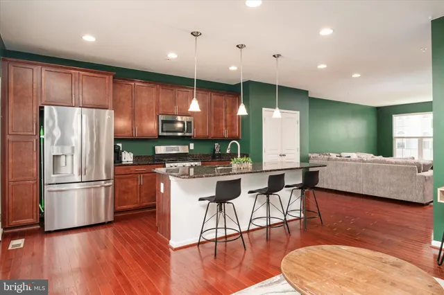a kitchen with stainless steel appliances kitchen island granite countertop a refrigerator a stove a sink a dining table and chairs with wooden floor
