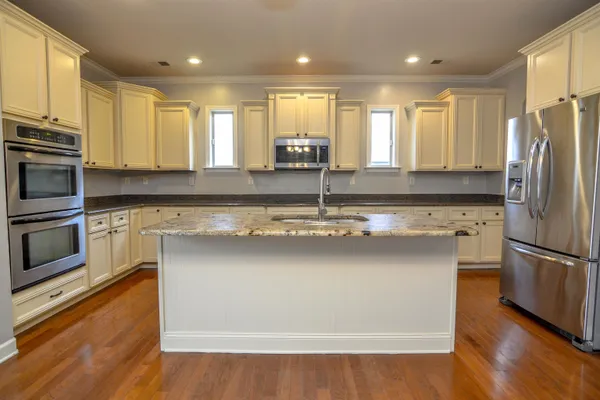 a kitchen with stainless steel appliances granite countertop a refrigerator a sink a stove and white cabinets with wooden floor