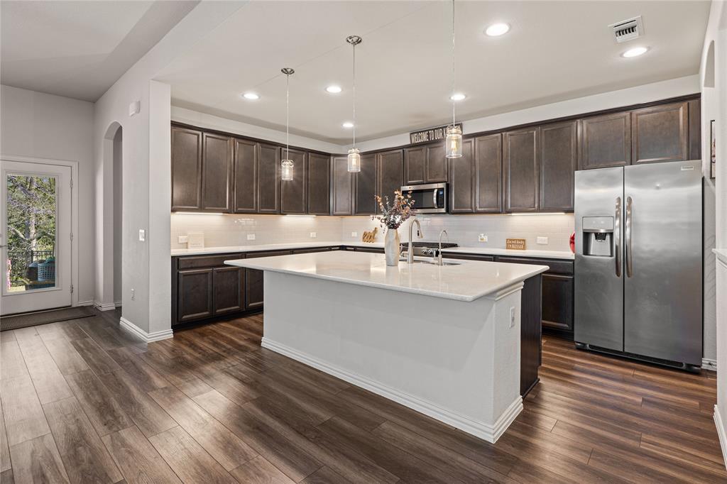 9517 Sunset Lane Oak Point, TX 75068 - Photo 14 of 40 9517 Sunset Lane, Oak Point, TX 75068 - kitchen - Kitchen with stainless steel appliances, dark wood finish cabinetry, arched walkways, a center island with sink, and decorative light fixtures