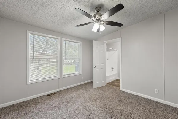 an empty room with chandelier fan and windows