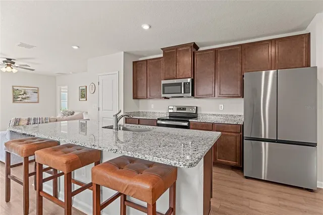 a kitchen with stainless steel appliances granite countertop a refrigerator a stove a sink a dining table and chairs