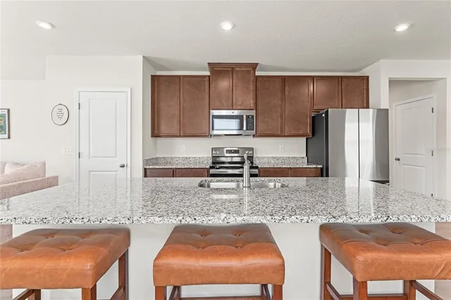 a kitchen with stainless steel appliances granite countertop a sink refrigerator and chairs