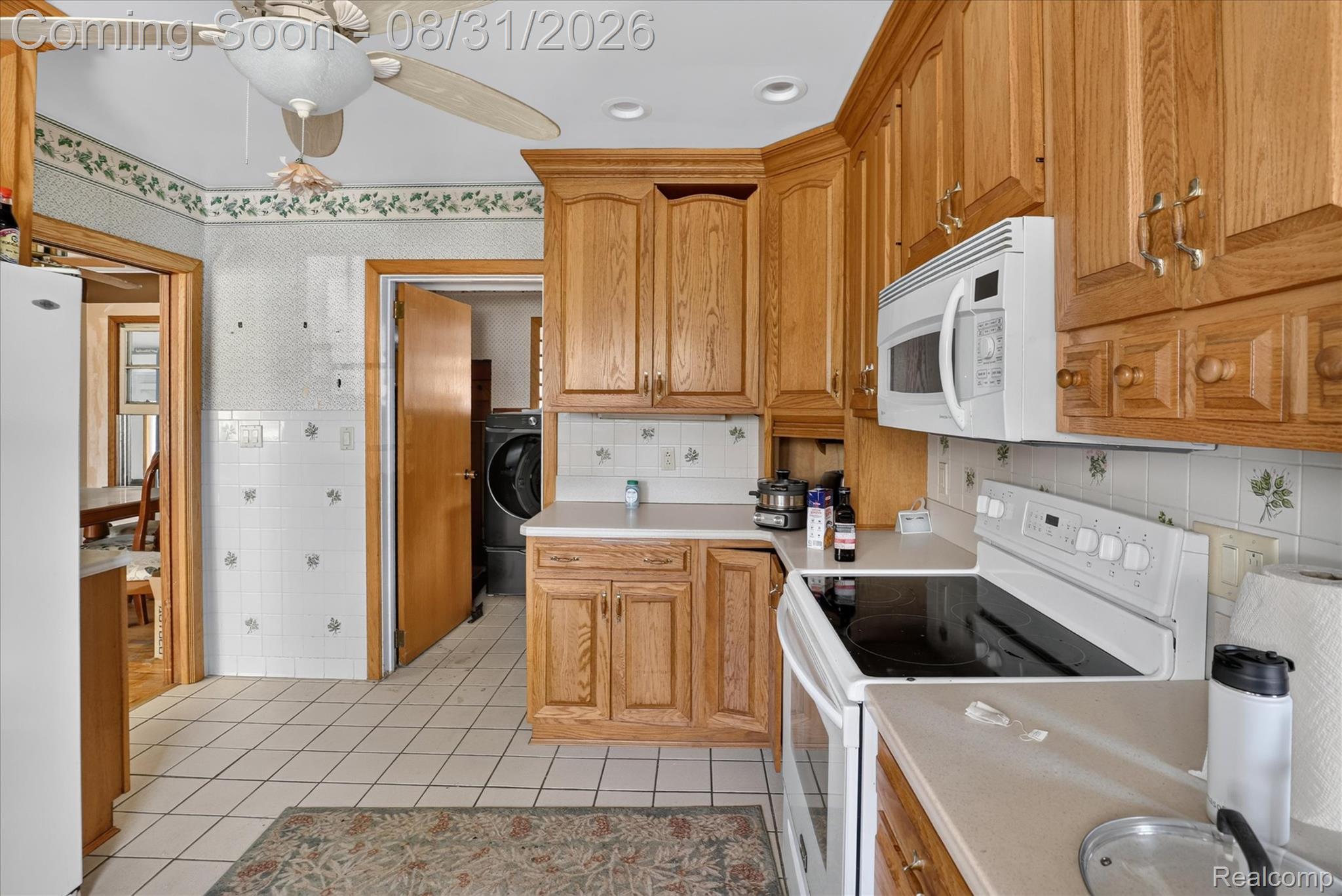 10165 Talladay Road Willis, MI 48191 - Photo 19 of 56 Wood-finish cabinetry, white tile flooring, white tile backsplash, white countertop, and white range with coordinating microwave