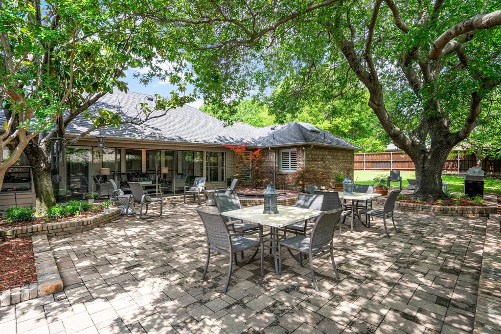 a view of patio with table and chairs under an umbrella with large trees
