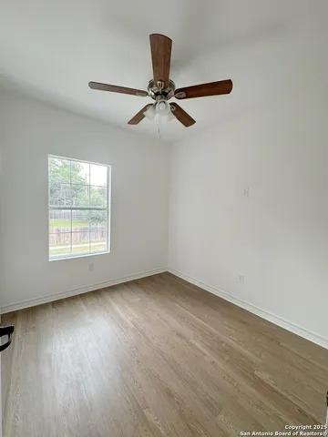 an empty room with wooden floor fan and windows
