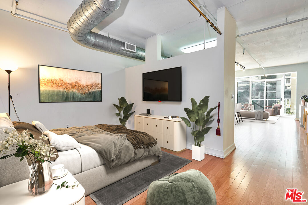 a bedroom with bed a flat tv screen and a potted plant