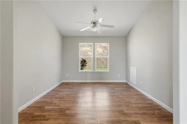 an empty room with wooden floor chandelier fan and windows