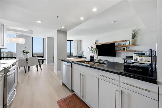 a kitchen with stainless steel appliances a sink dishwasher a stove refrigerator and a dining table with wooden floor