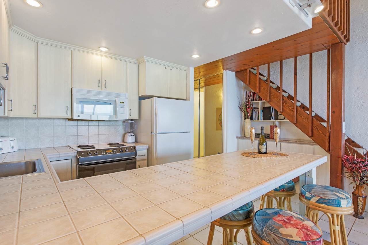 3543 Lower Honoapiilani Road, Unit F405 Lahaina, HI 96761 - Photo 19 of 30 a kitchen with stainless steel appliances kitchen island granite countertop a refrigerator a stove a sink and a dining table with wooden floor