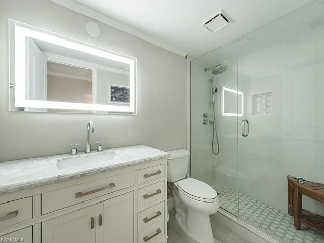 a bathroom with a granite countertop toilet a sink a mirror and shower