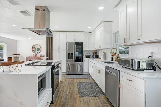 a kitchen with stainless steel appliances granite countertop a stove top oven a sink dishwasher a refrigerator and white cabinets with wooden floor
