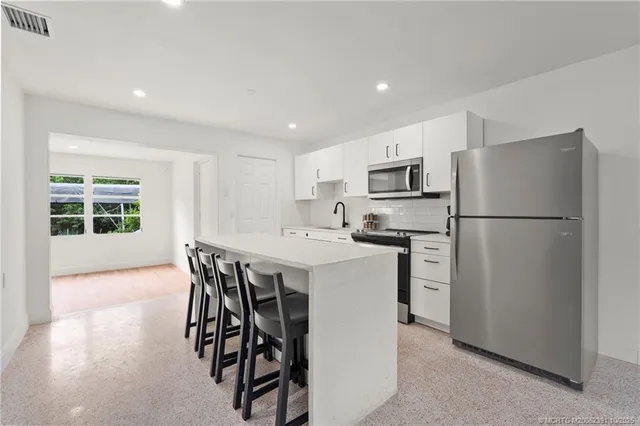 a kitchen with stainless steel appliances kitchen island granite countertop a stove a sink a refrigerator a dining table and chairs with wooden floor