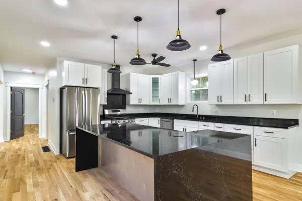 a kitchen with stainless steel appliances granite countertop a sink a stove a refrigerator and island with wooden floor