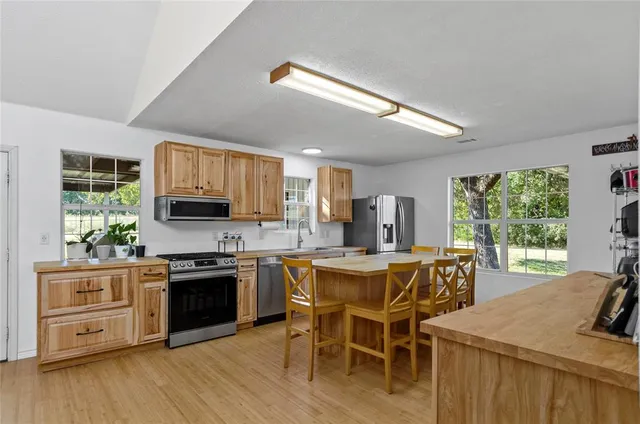 a kitchen with stainless steel appliances granite countertop a stove top oven a sink dishwasher a dining table and chairs with wooden floor