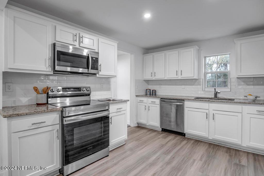 4623 Ribault Park Street Jacksonville, FL 32233 - Photo 12 of 30 a kitchen with granite countertop white cabinets stainless steel appliances and wooden floor