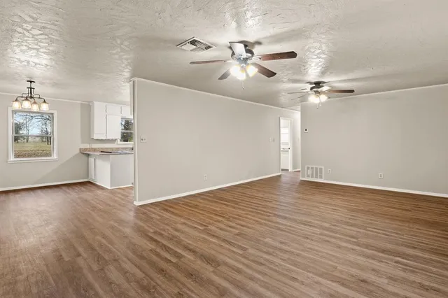 an empty room with wooden floor fan and windows