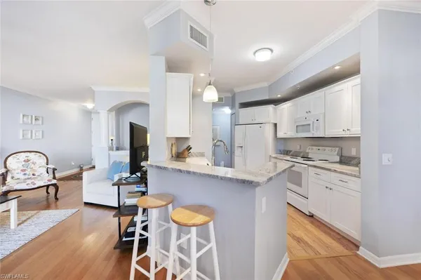 a living room with stainless steel appliances furniture a rug kitchen view and a table