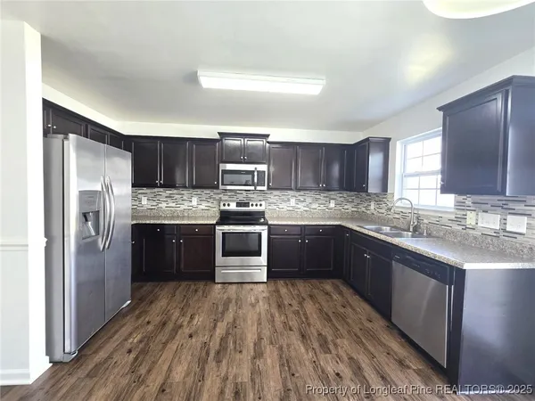 a kitchen with stainless steel appliances granite countertop a refrigerator a sink dishwasher a stove with wooden cabinets and floor