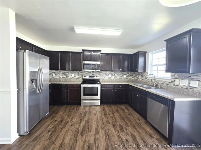 a kitchen with stainless steel appliances granite countertop a refrigerator a sink dishwasher a stove with wooden cabinets and floor