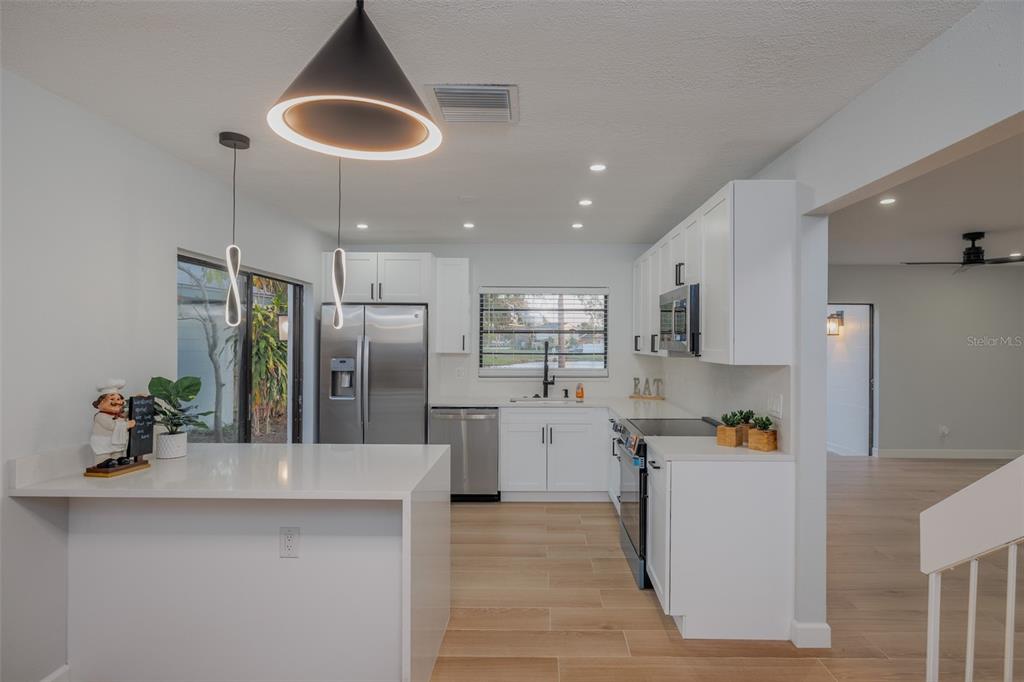 11033 Springridge Drive Tampa, FL 33624 - Photo 3 of 33 a kitchen with stainless steel appliances kitchen island granite countertop a refrigerator a sink a stove and white cabinets with wooden floor