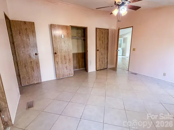 an empty room with chandelier fan and kitchen view