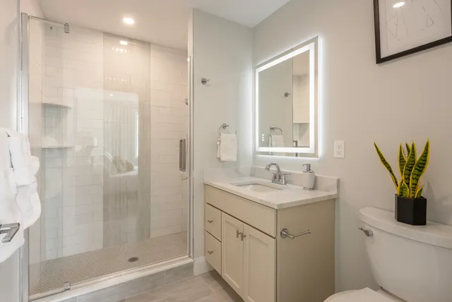 a bathroom with a granite countertop sink a mirror a shower and a toilet