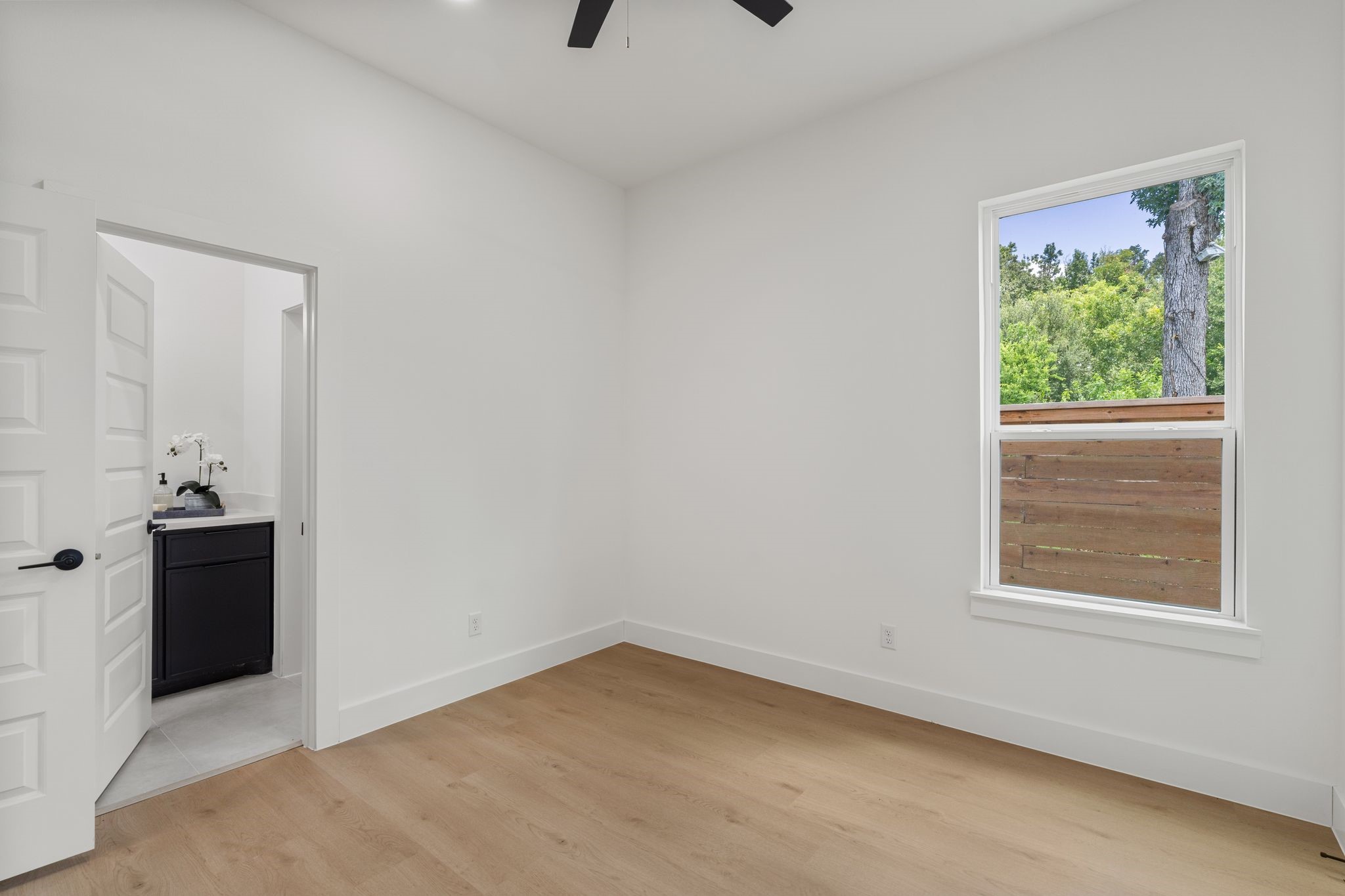 7321 Laura Koppe Road Houston, TX 77028 - Photo 31 of 41 Bright, airy room with sleek hardwood floors and
amodern ceiling fan, featuring a window with lush
green views and an adjacent bathroom with
contemporary fixtures.