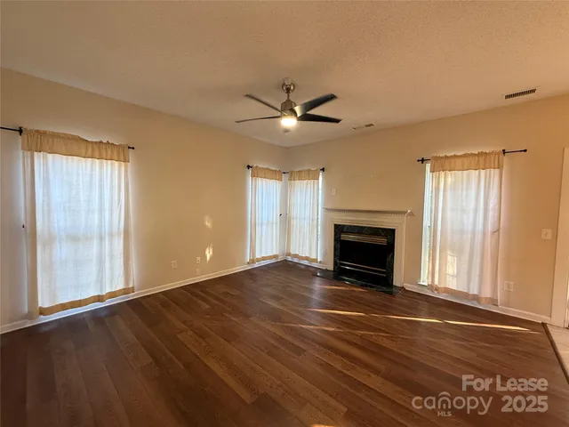 a view of an empty room with wooden floor fireplace and a window