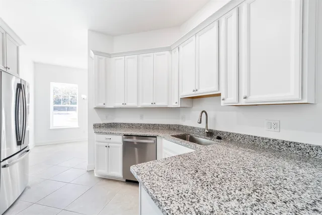 a kitchen with stainless steel appliances granite countertop a sink a stove a refrigerator and white cabinets with wooden floor