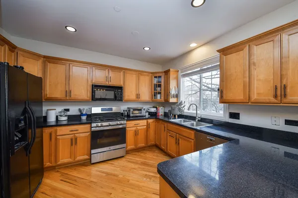 a kitchen with stainless steel appliances granite countertop wooden cabinets a sink dishwasher a stove and a refrigerator with wooden floor