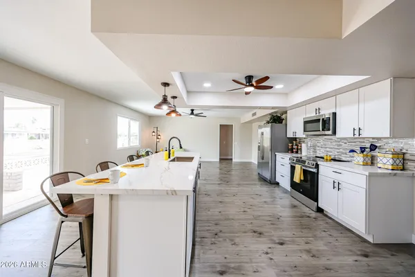 a open kitchen with stainless steel appliances kitchen island granite countertop a refrigerator a stove top oven a sink dishwasher and white cabinets with wooden floor