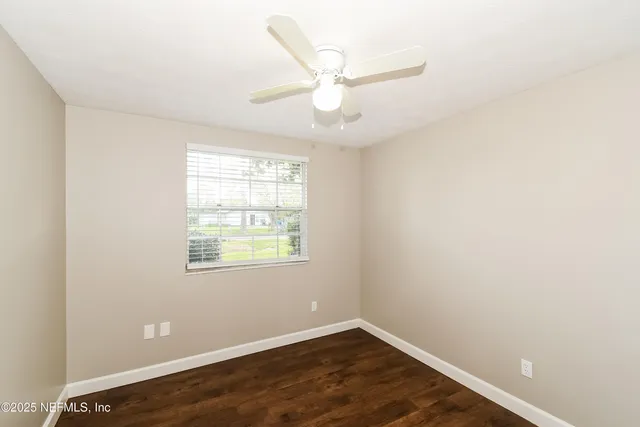 an empty room with wooden floor fan and windows
