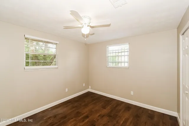 an empty room with wooden floor closet and windows