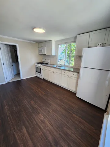 a kitchen with a refrigerator a stove a sink and white cabinets with wooden floor