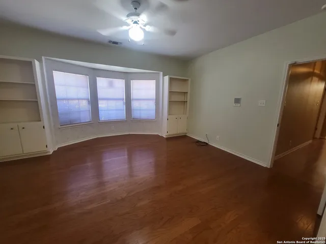 a view of empty room with wooden floor and fan