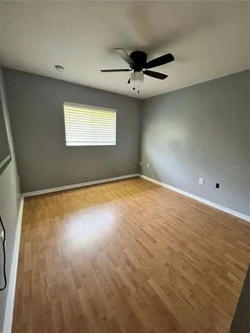 an empty room with wooden floor chandelier fan and windows