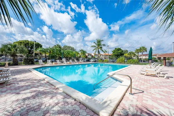 a view of swimming pool that has lawn chairs plants and palm trees