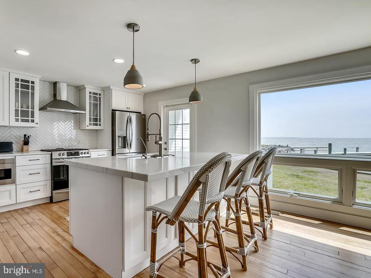 21642 Chicken Point Road Tilghman, MD 21671 - Photo 15 of 63 a open kitchen with stainless steel appliances granite countertop a stove top oven a sink a dining table and chairs with wooden floor