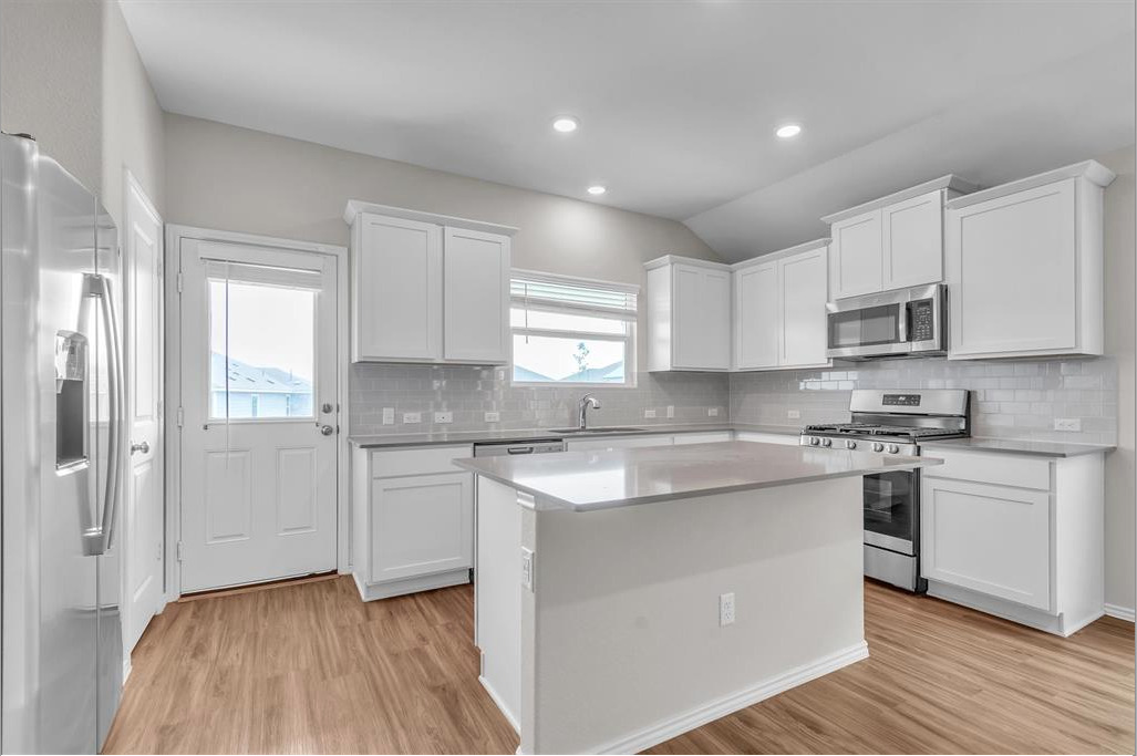 240 Madrid Kyle, TX 78640 - Photo 4 of 25 Kitchen with stainless steel appliances, light wood finished floors, healthy amount of natural light, white cabinets, and lofted ceiling