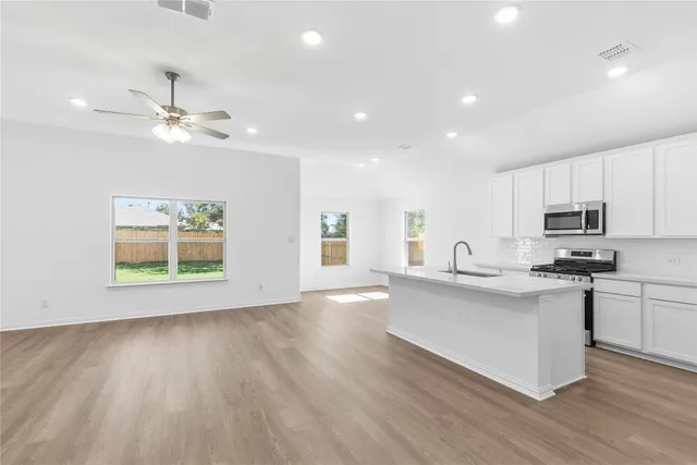 a view of kitchen with stainless steel appliances granite countertop a stove top oven a sink with wooden floors