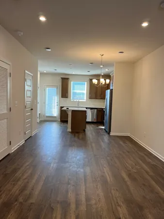 an empty room with wooden floor and kitchen view