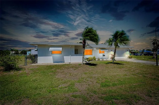a view of yellow house with a big yard potted plants and palm trees
